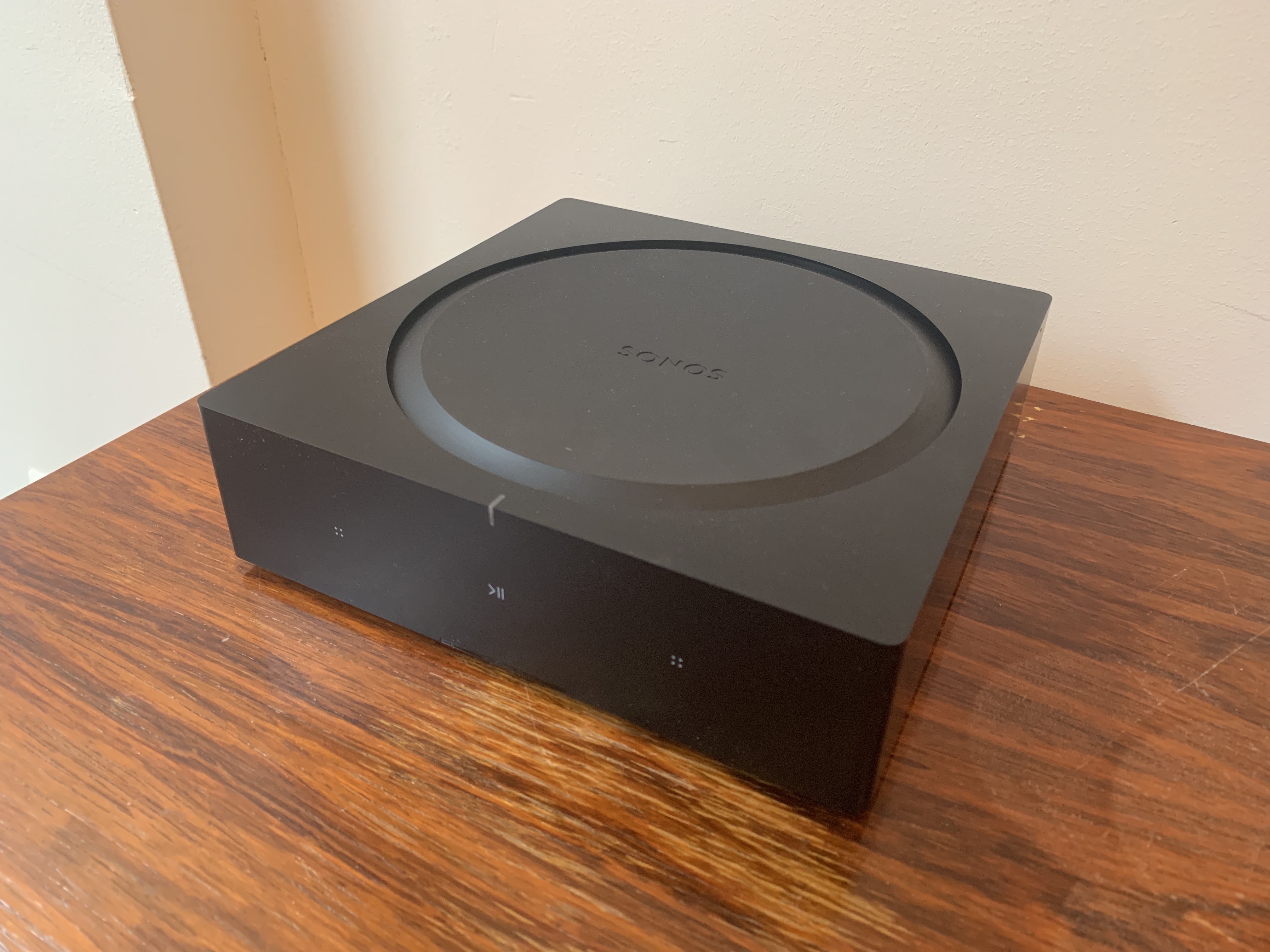 A black Sonos Amp on a wooden surface.