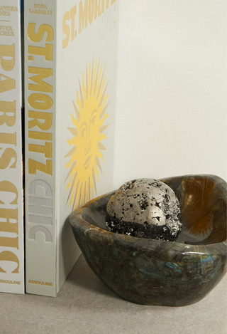 A pyrite crystal ball in a bowl beside Assouline books