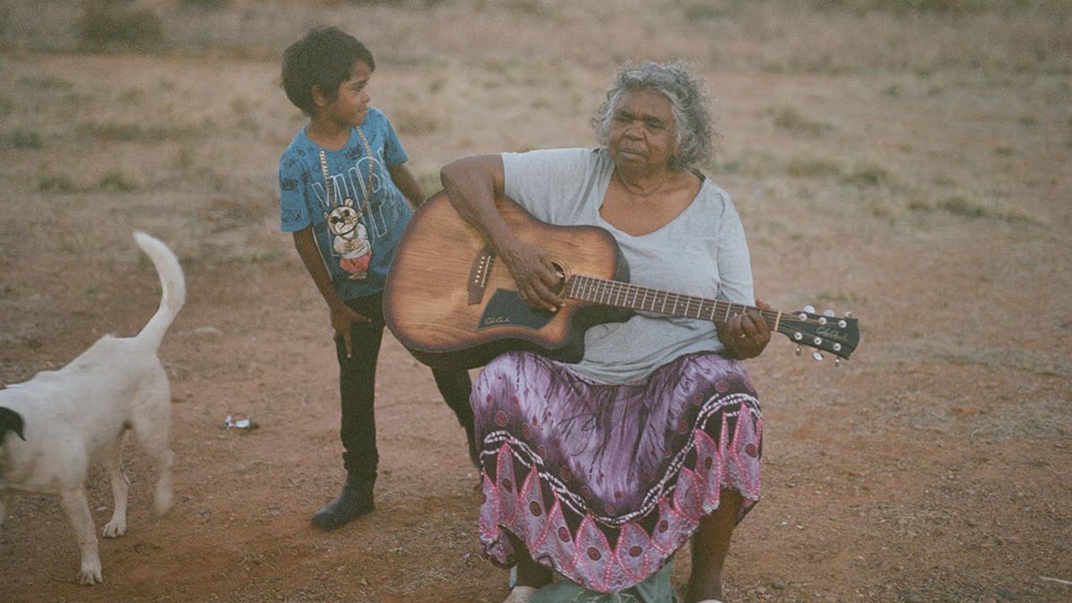 Kankawa Nagarra playing guitar next to a child and a dog