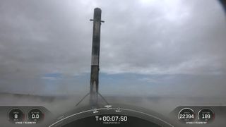 black and white spacex rocket rests on a landing pad beneath a cloudy sky