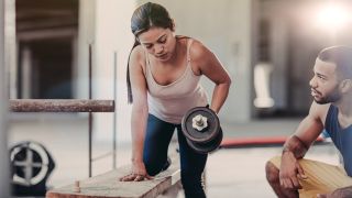 Woman performs one-arm dumbbell row under instruction of trainer