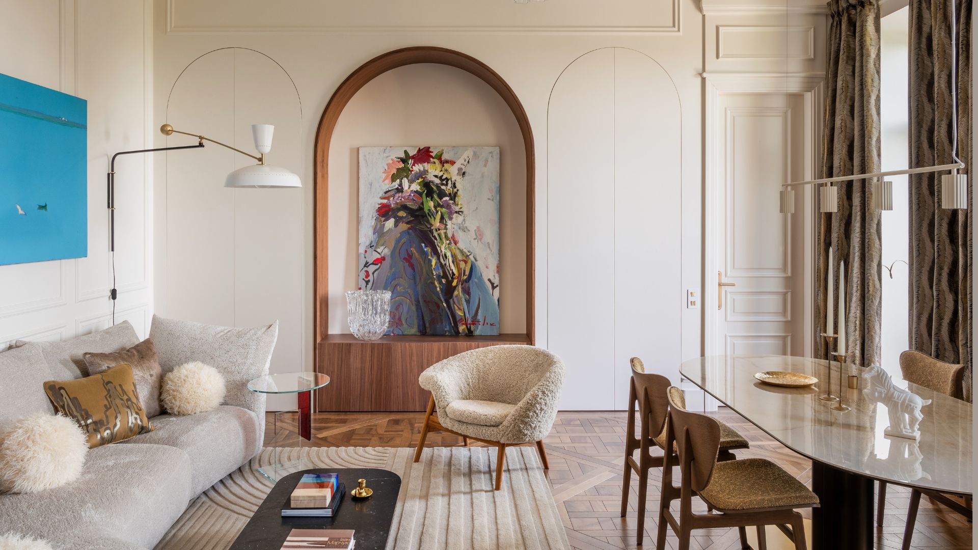 A living room and ding space in a contemporary home with wood flooring, curved nooks, framed art, floor lamps, a sofa and plush sofa seater with a rug