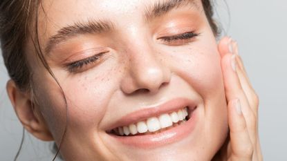 Close up studio shot of a woman with smooth, glowing skin, touching her face and smiling after using ceramides
