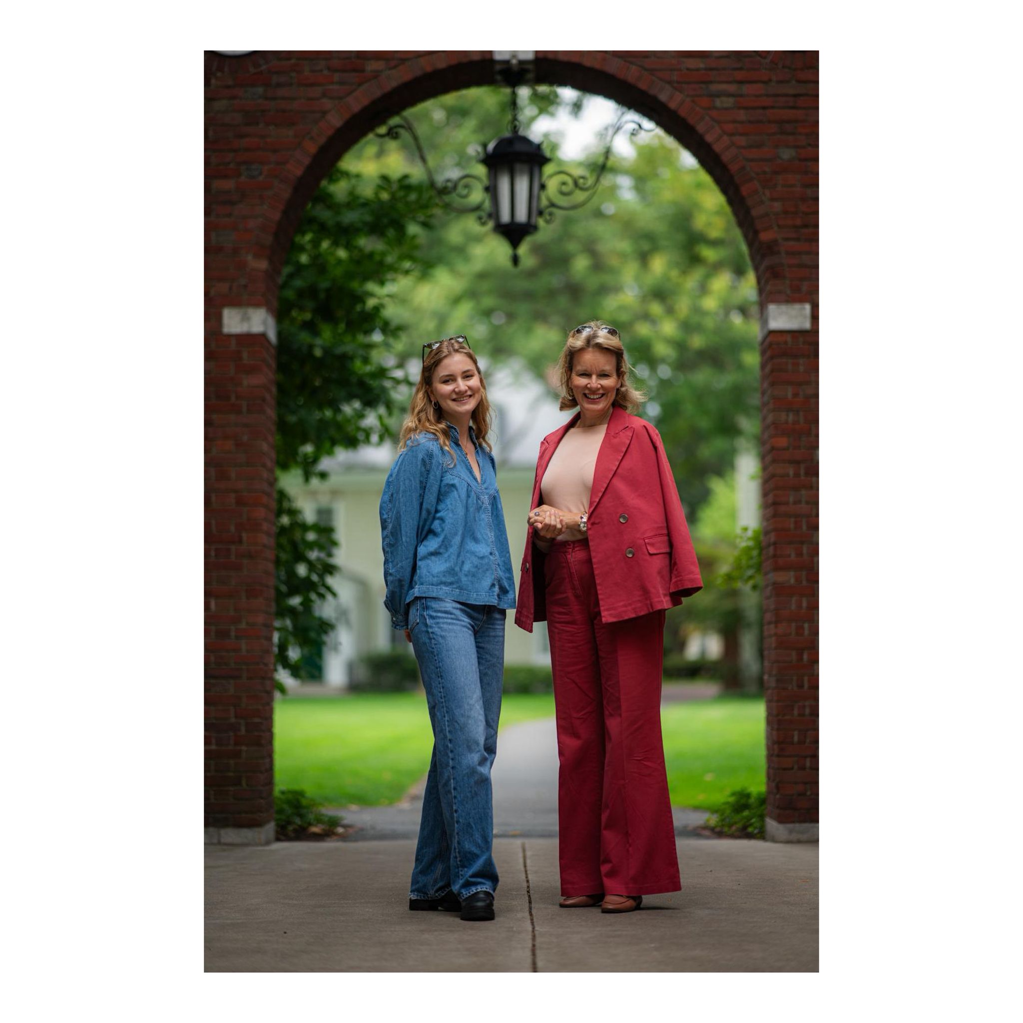 Princess Elisabeth wearing jeans and Queen Mathilde in a pink suit posing under an archway at Harvard