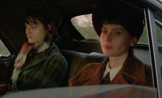 raffey cassidy and felicity jones riding in a car in 50s era clothing in a still from the brutalist