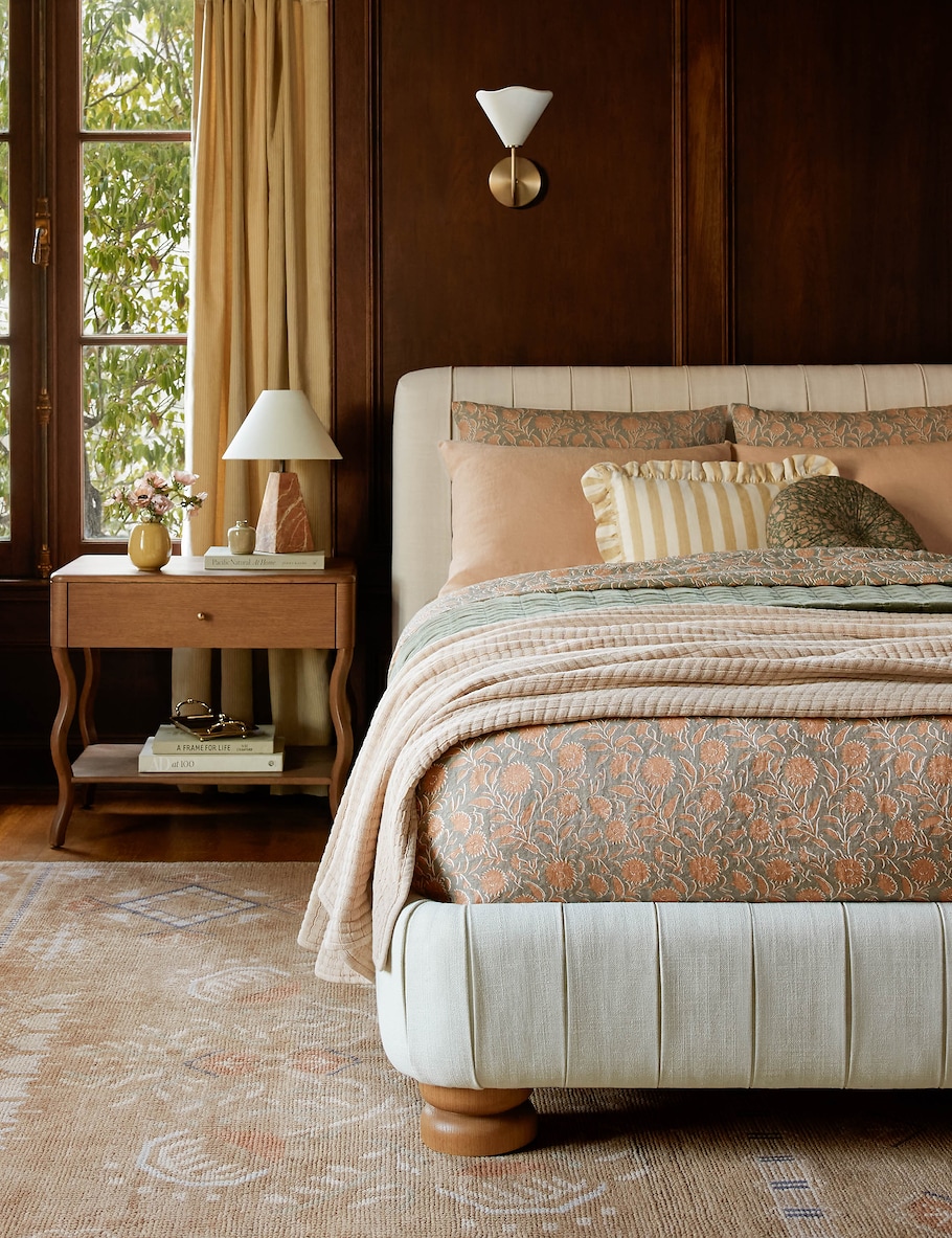 room with a bed with sheets and pillows of varying patterns, a tan rug and wooden walls