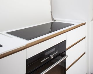 A close-up shot of a narrow induction hob above white kitchen cabinets and a built-in oven
