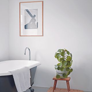 Bathroom with freestanding black bath, wooden stool and framed art.