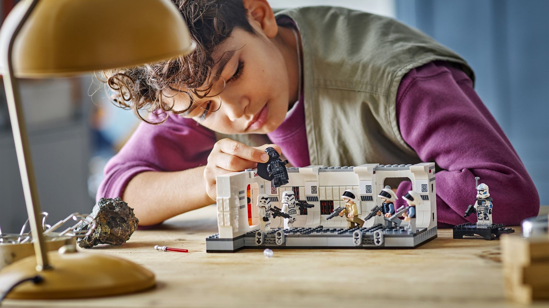 A boy playing with the Lego Boarding the Tantive IV, holding Darth Vader.