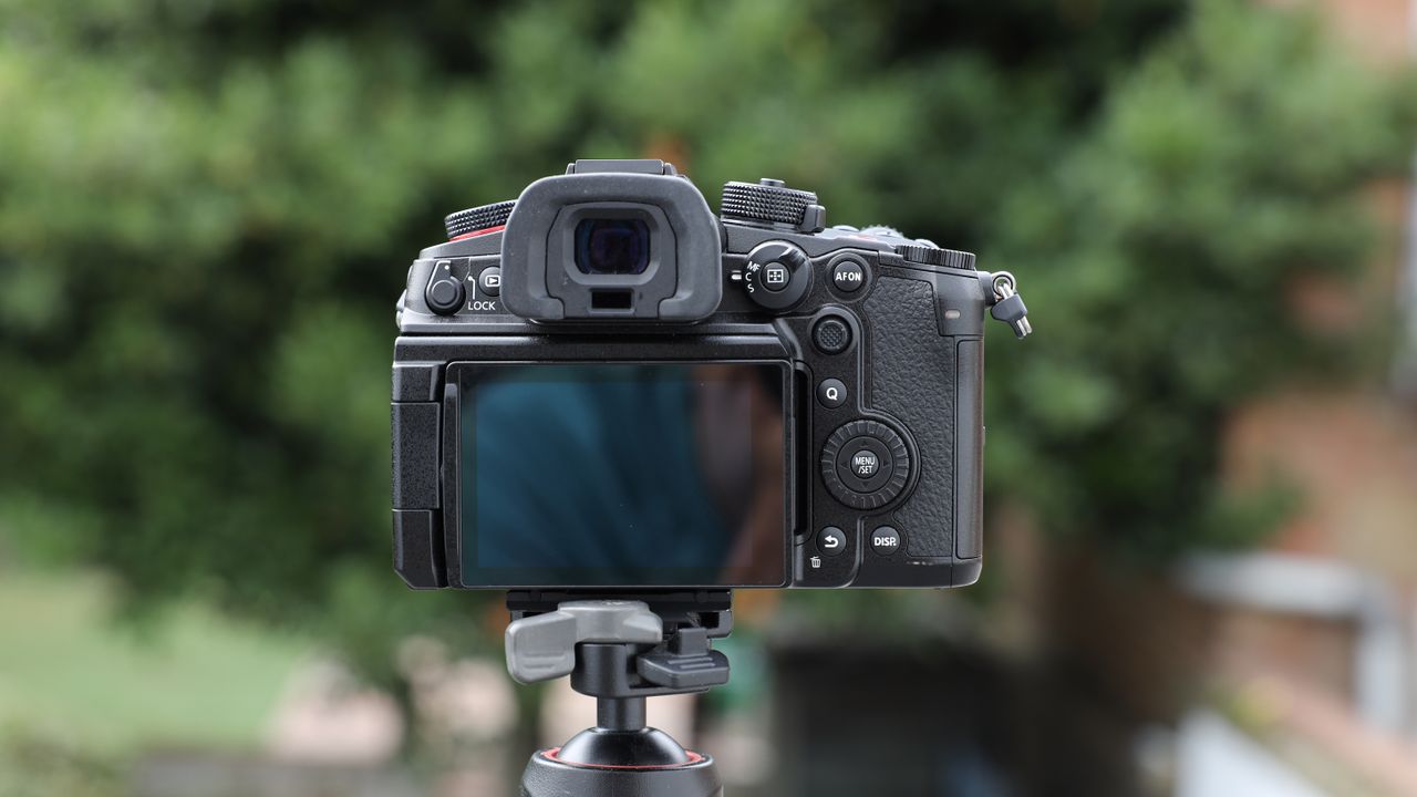 Panasonic Lumix GH7 on a tripod outside with some blurred green trees in the background