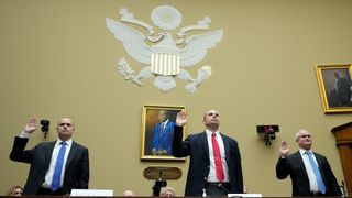 three men in suits raise their right hands in a large gold room