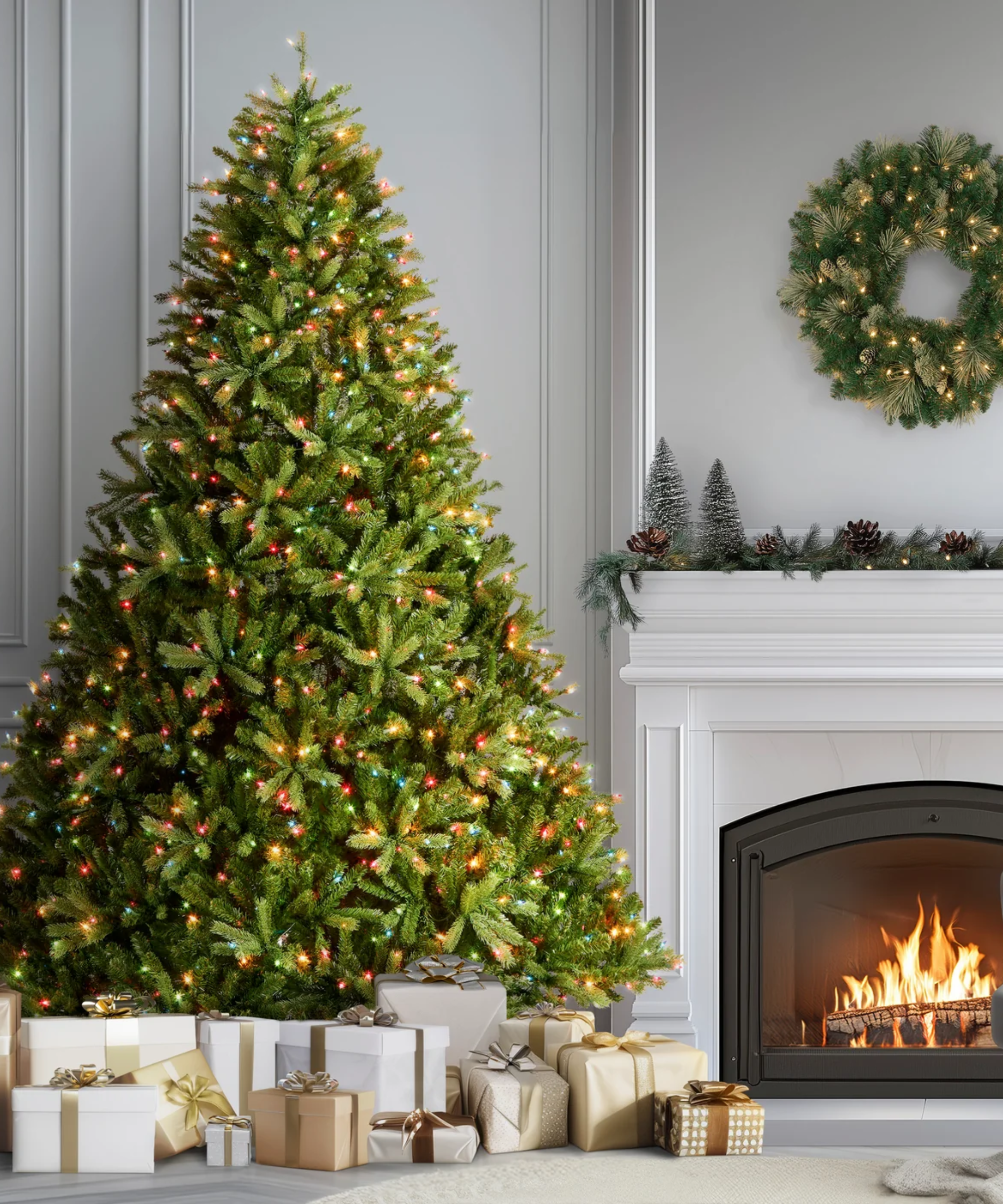 Festive holiday living room featuring a roaring fire alongside an oversized tree with multicolored lights and overflowing wrapped presents at the base.