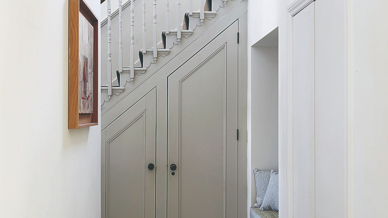 A narrow hallway with a staircase at the end and an under stairs storage cupboard with closed doors