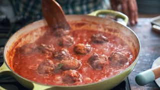 image shows person cooking pork meatballs with tomato sauce