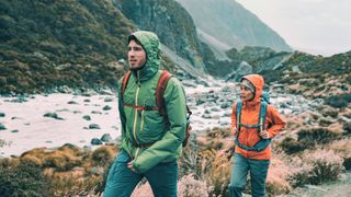 a photo of a man and woman hiking with their rain jacket hoods up