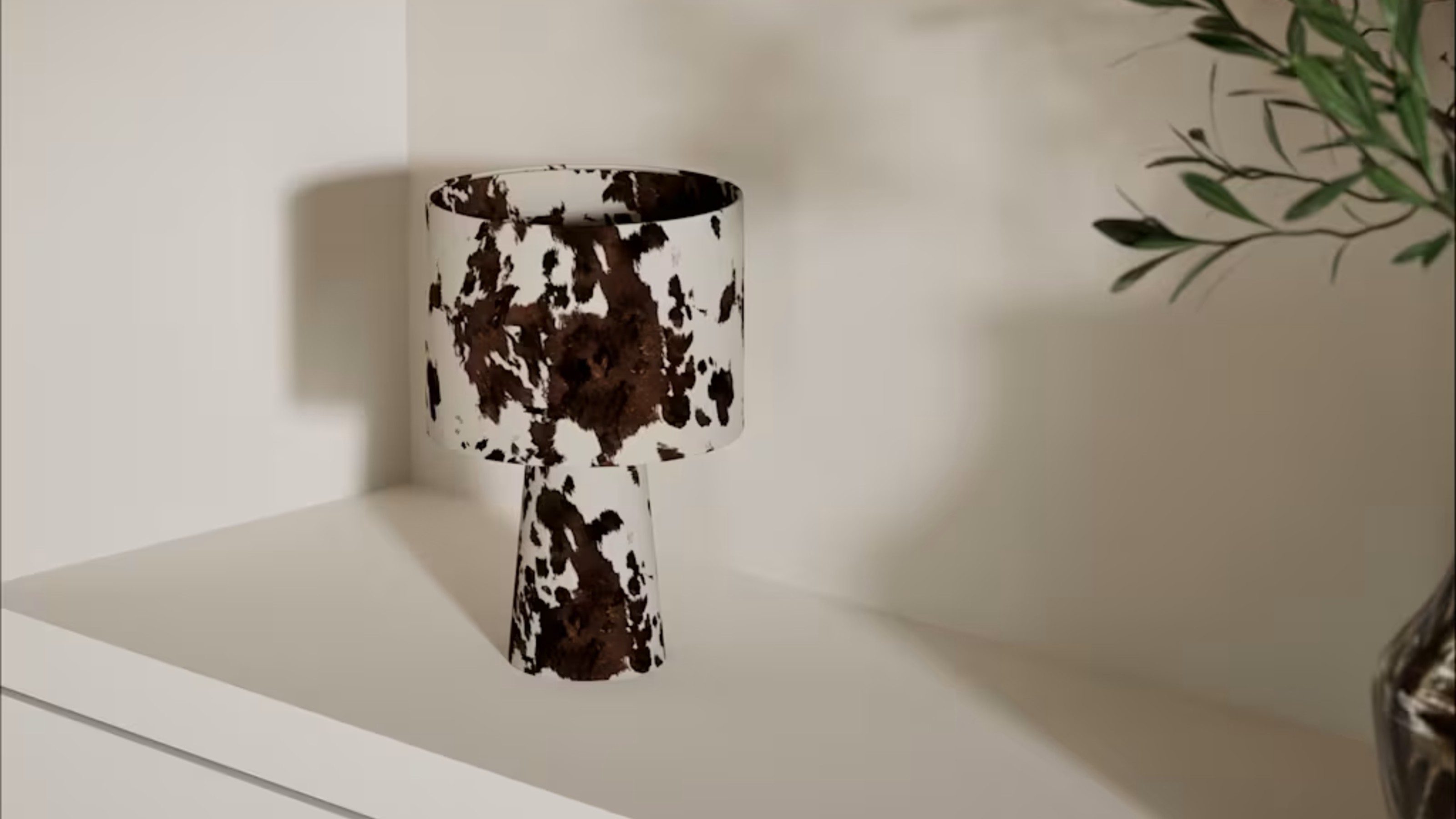 M&amp;S Fabric Cow Print Table Lamp on a shelf next to a vase of foliage