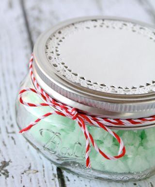 A mason jar with mint scrub made using coconut oil, mint extract, sugar and green food coloring with paper doily and red/white twine decor