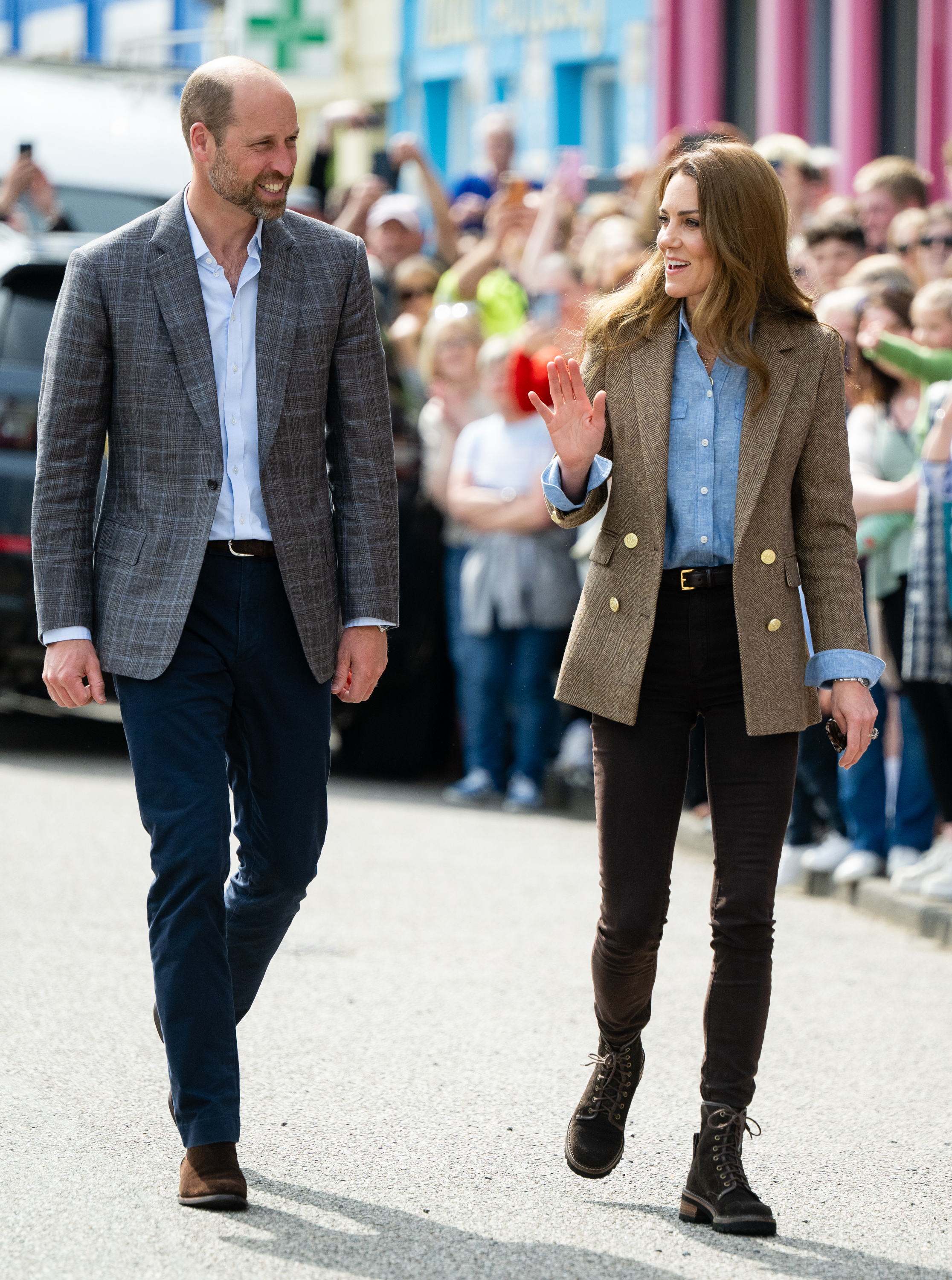 Prince William and Princess Kate walking down a street and waving in Scotland