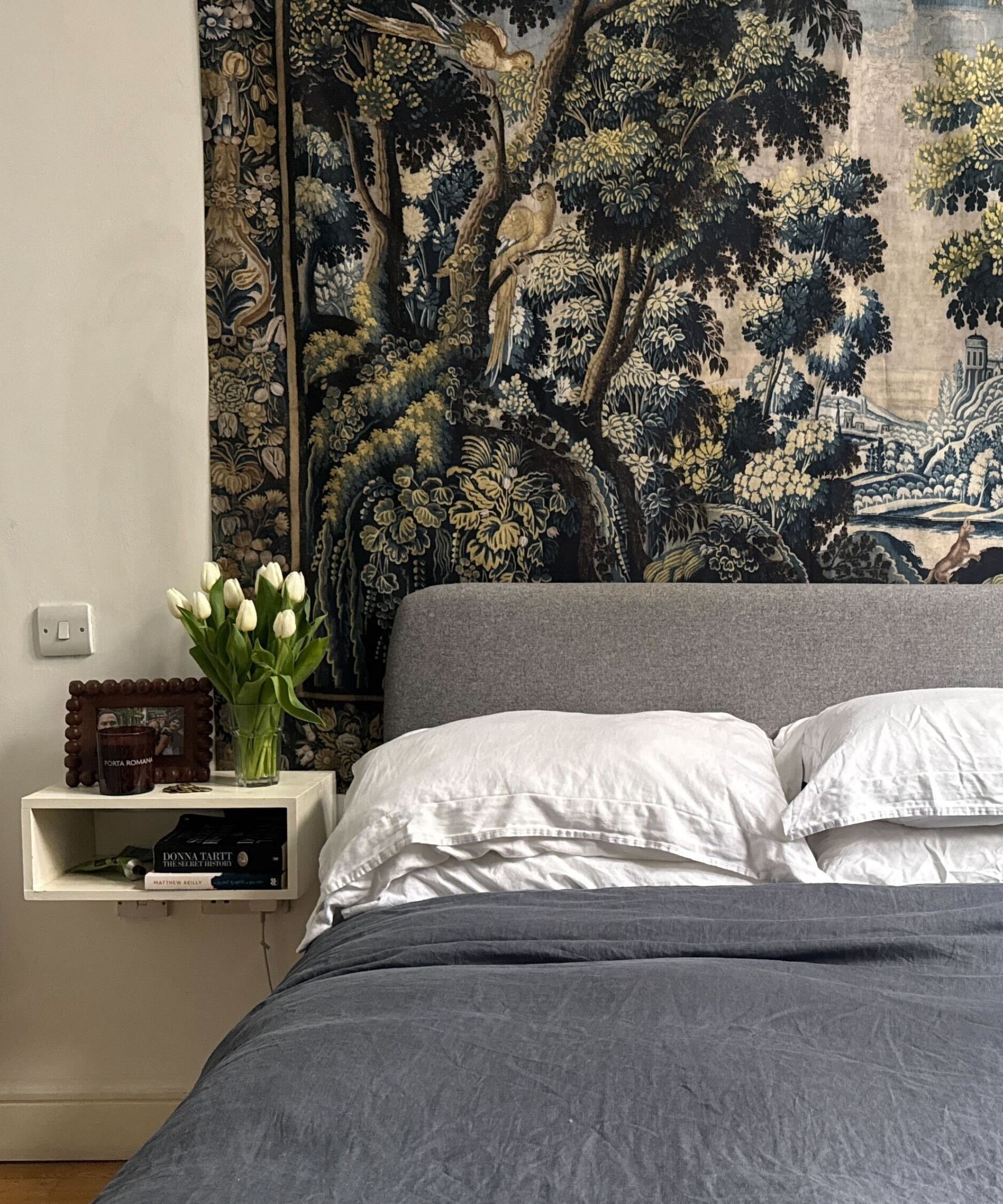 Pottery Barn Linen Bedding in bedroom with tapestry, side table with vase of tulips and picture frame