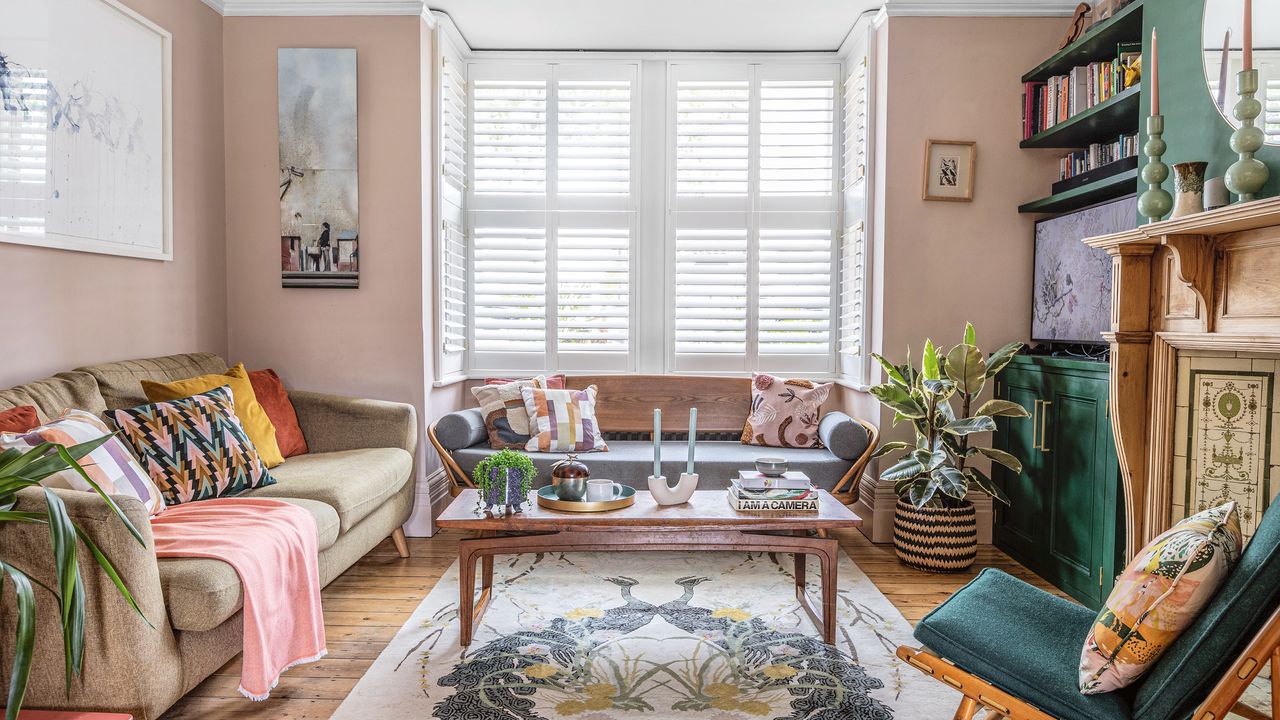 Pink living room with large patterned area rug and white shutters at the windows