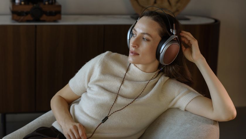 Woman in white, short-sleeved jumper relaxes at home in premium Meze Audio headphones.