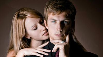 man in suit with woman behind him nuzzling his neck