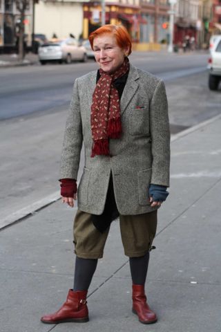 A photo of Alice Carey in an over 60 outfit featuring a black top, gray tweed blazer, green shorts, gray tights, red boots, and red scarf.