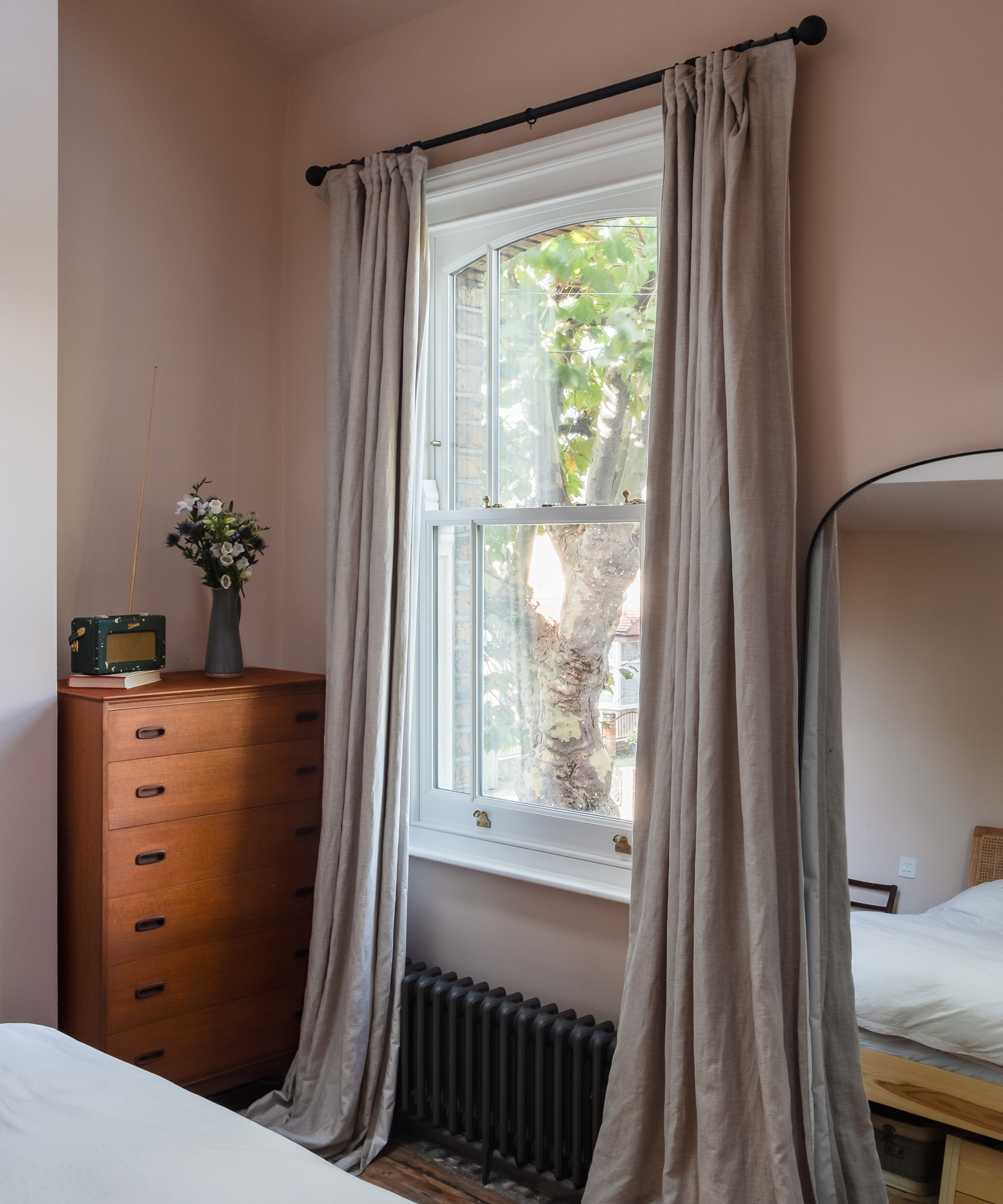 A window with long linen curtains and a set of wooden drawers to the left