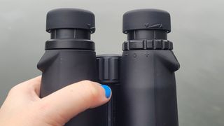 Celestron Outland X 10x42 binoculars in-hand, showing the diopter ring