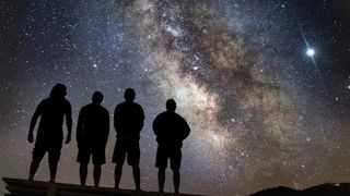 A group of people stand silhouetted in front of the night sky with the Milky Way on full display.