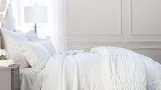 Bed in white bedroom with paneled walls, with white ruffled bedding