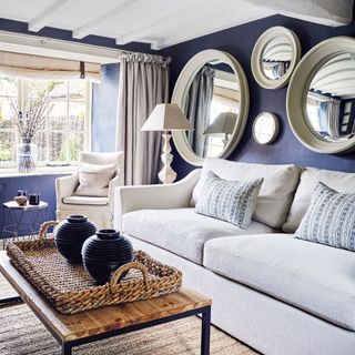 Ble living room with white ceiling and beams, white sofa and mirrors on wall