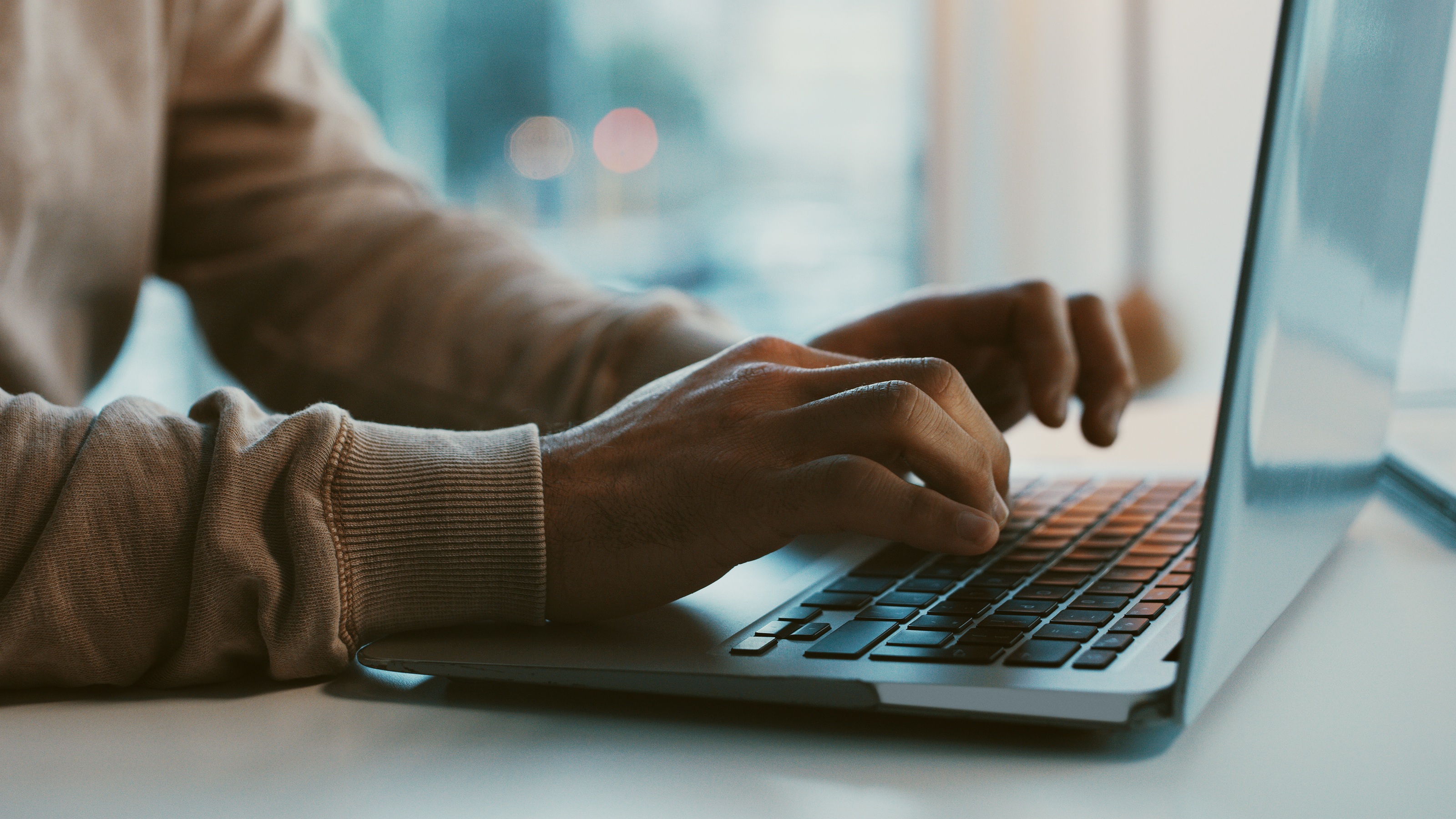 A man works on a laptop, only his hands and arms showing.