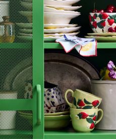 green kitchen cabinet with spring crockery, pots, utensils and fruit