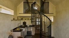 A tiny home with warm white limewash walls, a black spiral staircase, and a small kitchen with dark wood countertops