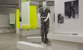 A mannequin modelling a black shirt and trousers with a crowd-style pattern. Information panels hang on yellow backgrounds