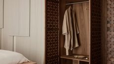 Image of a minimalist bedroom with a large, wooden built-in closet that is open and has a robe hanging in it.