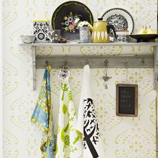 Wall shelf with china and hanging tea towels against patterned wallpapered wall