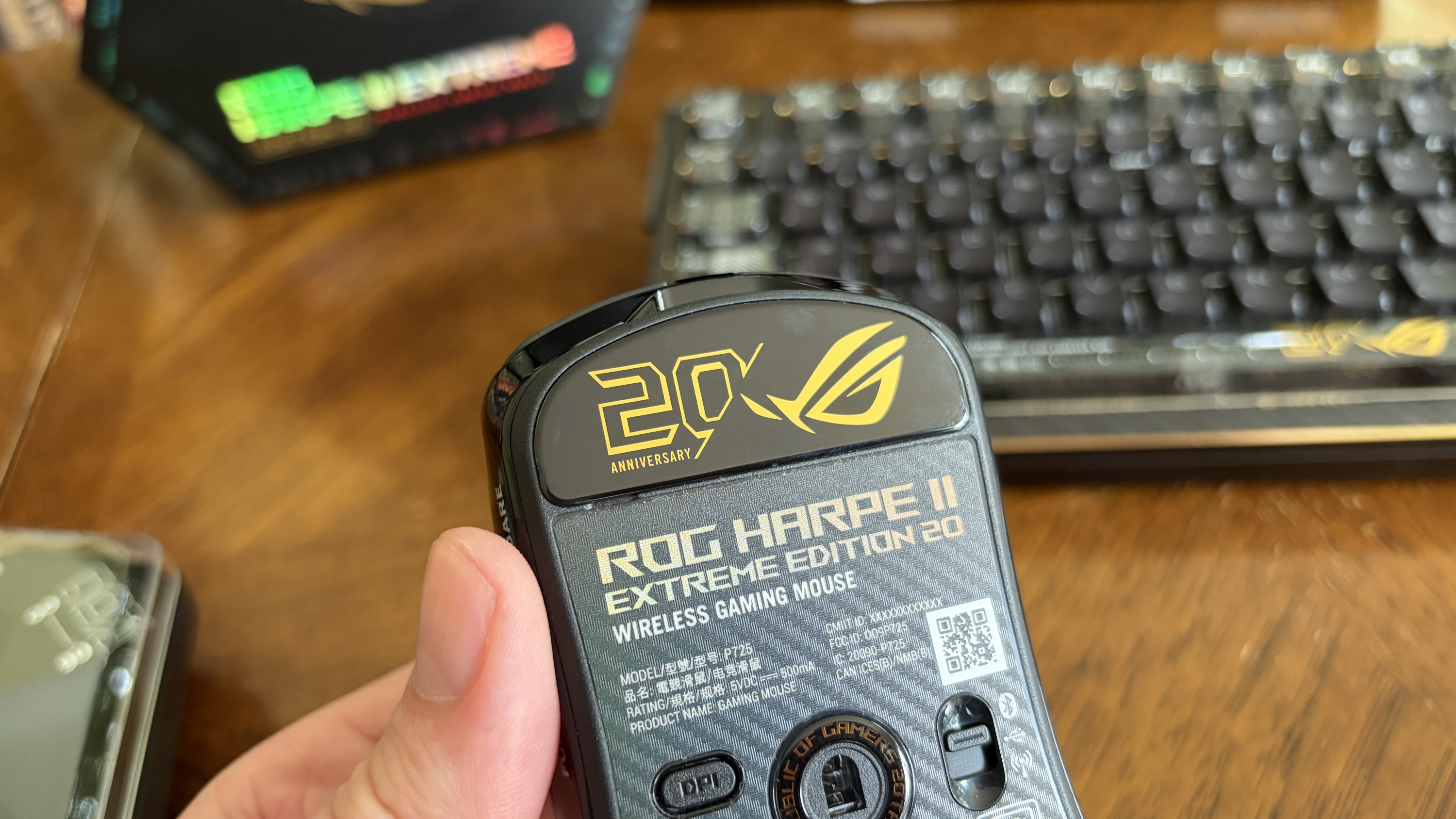 Underside of a ROG Harpe II Extreme Edition 20 wireless gaming mouse with anniversary emblem and text, held in a hand.