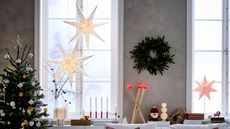 IKEA paper stars hung at the window of a living room with gray walls, a wreath between the window and a christmas tree decorated with white and gold