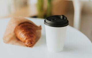 paper coffee cup and croissant in paper bag on white table