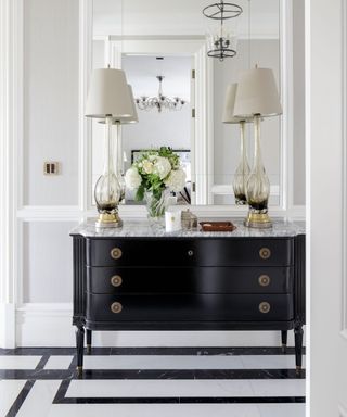 Classic hallway ideas shown in white, with a black console table and monochrome marble flooring.