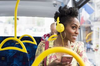woman travelling on a bus, looking out of the window and wearing yellow headphones