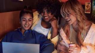 Three young women crowded around a laptop watch a TV show on Amazon Prime Video