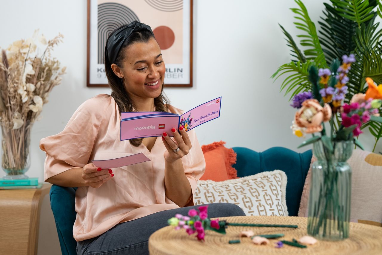 A smiling mum reads her Time Tokens for Mum free booklet from Moonpig and Lego