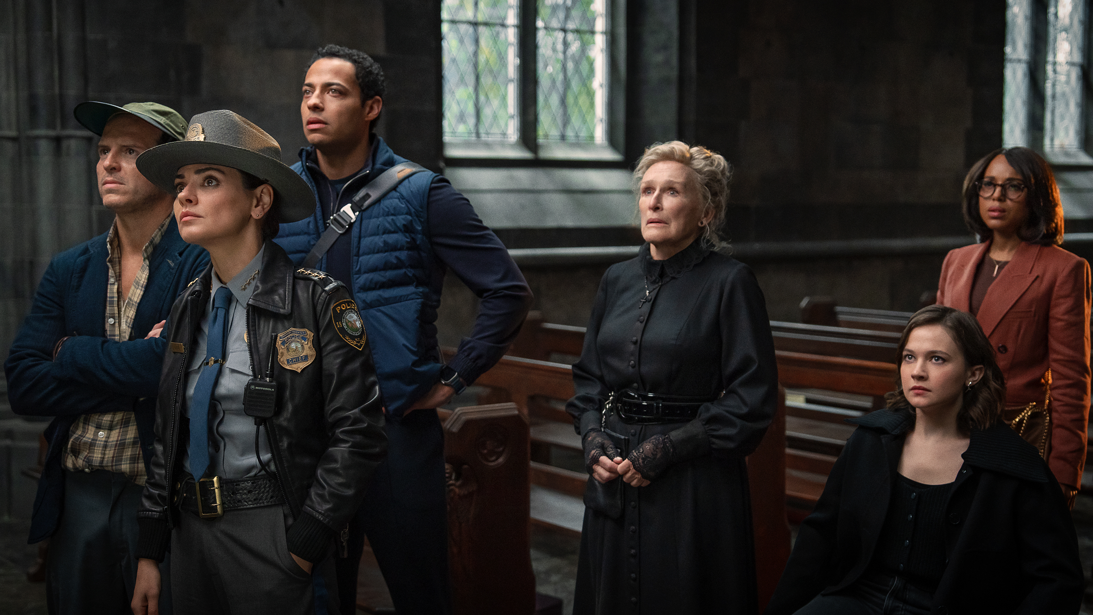 L-R: Andrew Scott, Mila Kunis, Daryl McCormack, Glenn Close, Cailee Spaeny, Kerry Washington in a church in a scene from 