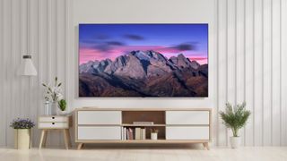 The LG B5 OLED displaying a mountain range at sunrise. The TV is wall-mounted in a bright, monochromatic living room setting above a credenza.