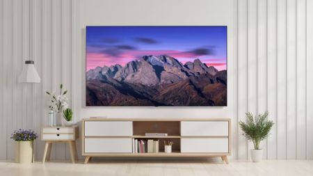 The LG B5 OLED displaying a mountain range at sunrise. The TV is wall-mounted in a bright, monochromatic living room setting above a credenza.