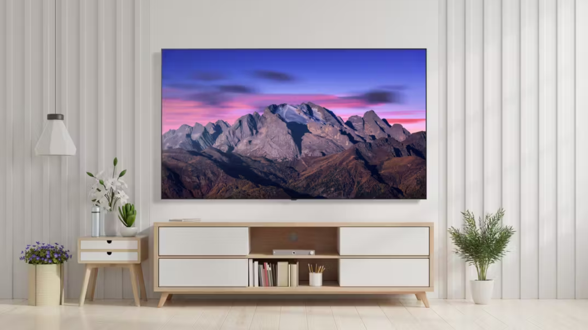 The LG B5 OLED displaying a mountain range at sunrise. The TV is wall-mounted in a bright, monochromatic living room setting above a credenza.