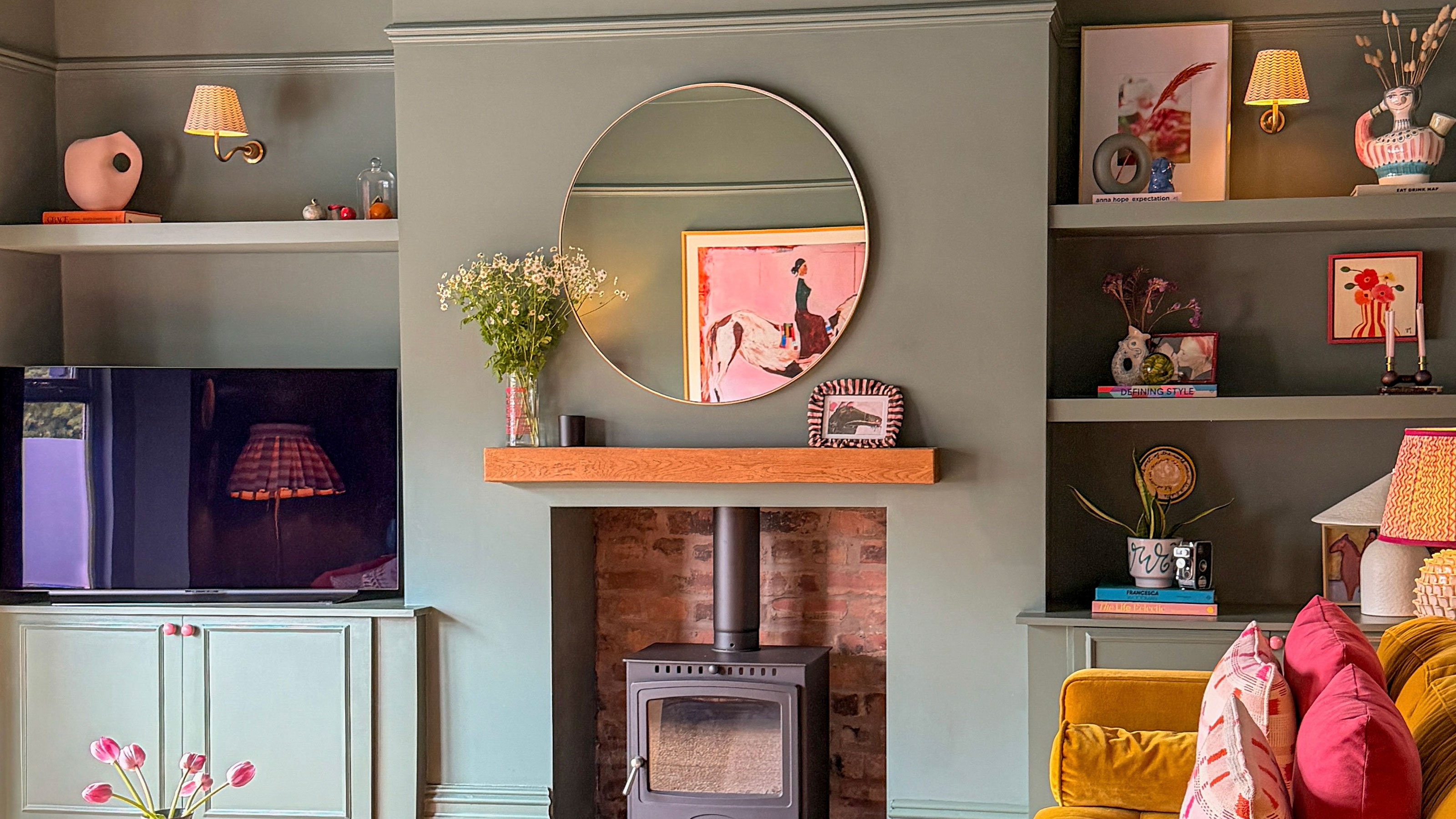 Green living room with built in cabinetry and bookshelves and log burner in fireplace